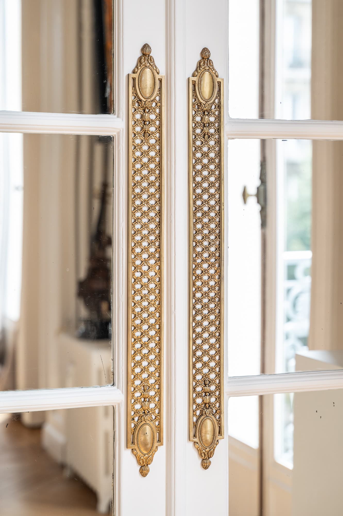 Poignées en bronze doré sur une double porte vitrée d’un appartement parisien